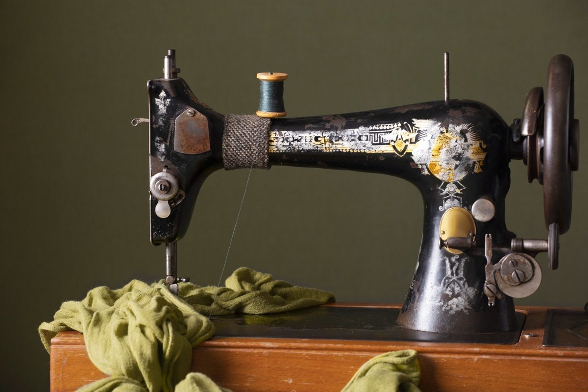Vintage black Singer sewing machine with gold detailing, green thread spool, and large handwheel on a wooden sewing table