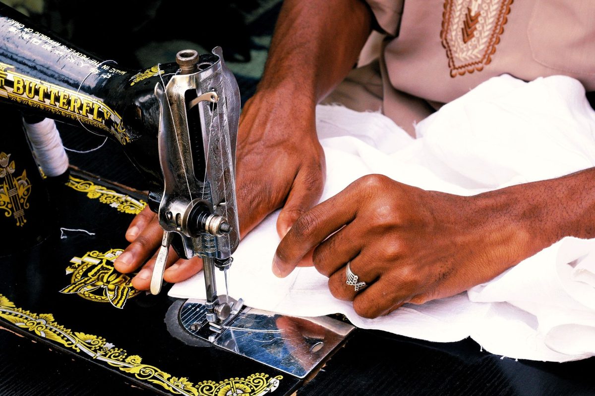 Tailor using a vintage Butterfly sewing machine to stitch white fabric.